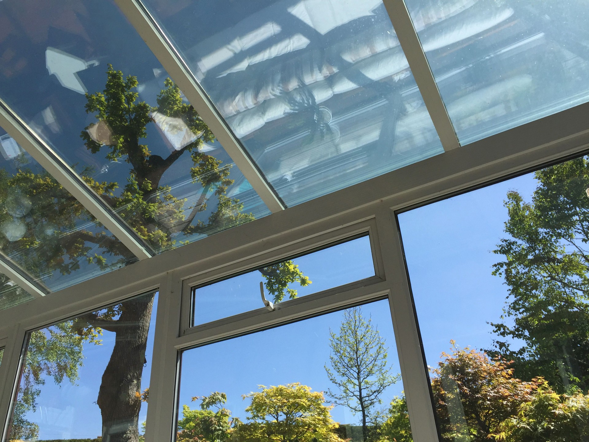 Image of rectangular white UPVC conservatory with glass roof of self-cleaning glass window panes tinted to keep conservatory cool in hot summer weather and not overheating, double-glazed windows with views of landscaped garden trees and sunny blue sky