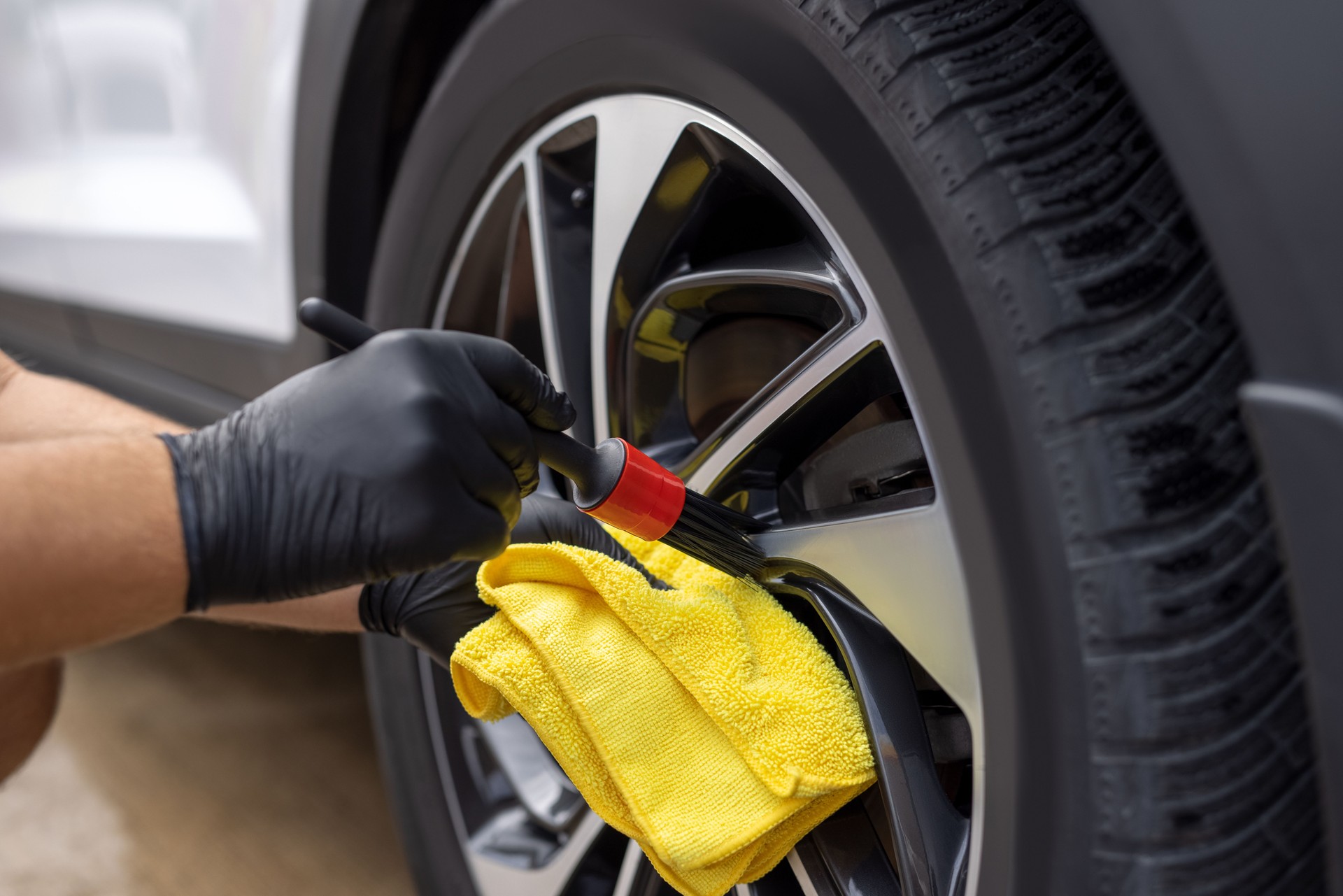 Unrecognizable car detailer cleaning car wheel with a brush